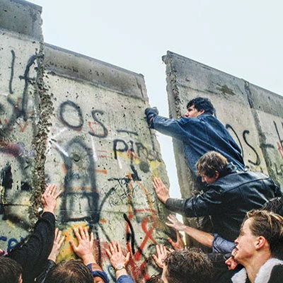 On November 9th East German guards begin allowing people to move through checkpoints at the Berlin Wall without checking identification. Over the next few weeks West Germans citizens begin breaking apart the wall and taking souvenirs, creating several new crossing points. In 1990 the wall is officially demolished and German reunification takes place.